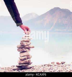 Homme pyramide construite à partir de galets. Pierre pyramide équilibrée sur le rivage de l'eau bleu de lac de montagne. Les montagnes bleues du niveau de l'eau miroir. mauvais éclairage Banque D'Images