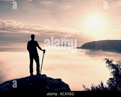 Guide touristique de hauteur sur la roche avec mât de pair avec l'équipement sportif randonneur. au-dessus de la vallée brumeuse. sunny spring daybreak en montagnes rocheuses. Banque D'Images