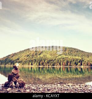 Pierre pyramide équilibrée sur le rivage de l'eau bleu de lac de montagne. Les montagnes bleues du niveau de l'eau miroir. De mauvaises conditions d'éclairage. Banque D'Images