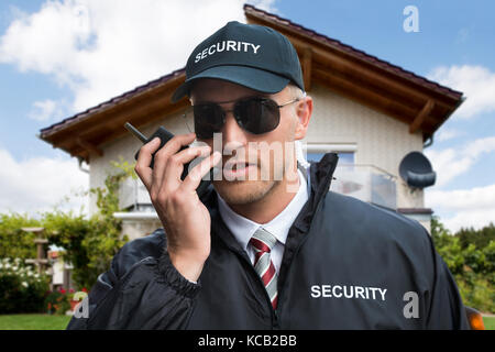 Close-up of a young male gardien de sécurité à l'aide de talkie-walkie devant une maison Banque D'Images