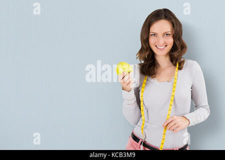 Portrait d'une jeune femme avec un ruban à mesurer et de pomme verte sur fond de couleur Banque D'Images