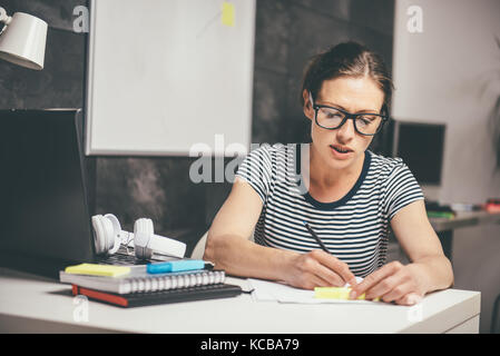 Woman wearing eyeglasses travailler tard au bureau et à l'écriture Banque D'Images