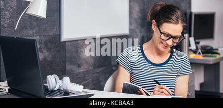 Woman wearing eyeglasses travailler tard au bureau et à l'écriture Banque D'Images