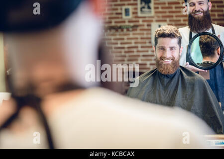 Jeune homme souriant en regardant sa nouvelle coupe de cheveux à la mode dans le Banque D'Images