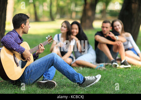 Le chant de l'homme chanson avec guitare à ses amis de parc sur chaude journée ensoleillée. les jeunes puissent profiter de chaque compagnie d'autres, beau temps et s'amuser. week-end, acc Banque D'Images