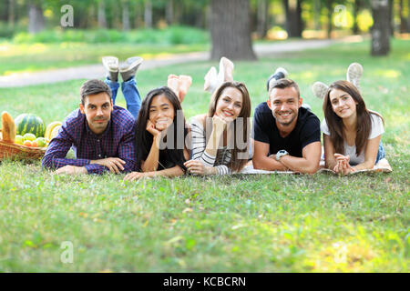 Les jeunes femmes et hommes d'origine ethnique différente de s'amuser ensemble. Cinq personnes lying on grass in row, smiling and looking at camera. meilleurs amis relaxine Banque D'Images