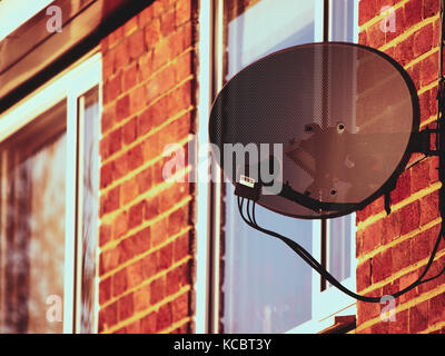 Antenne satellite sur le côté d'une maison en brique au coucher du soleil. Banque D'Images