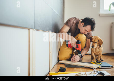 L'homme faisant des travaux de rénovation à la maison avec son petit chien jaune Banque D'Images