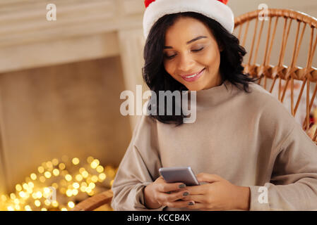 Femme agréable à santa hat texting avec mari Banque D'Images