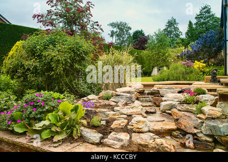 Un jardin de rocaille nouvellement plantées après l'installation d'une main-construit en pierre naturelle cascade dans un jardin anglais en UK Banque D'Images