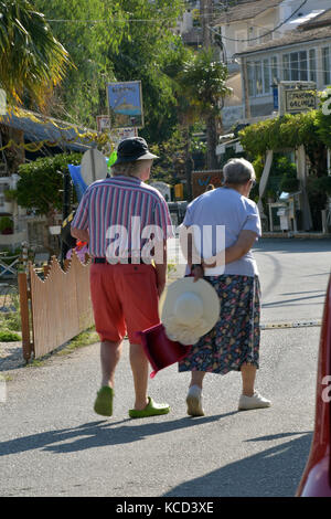 Un couple de personnes âgées de marcher le long d'une rue l'un portant un chapeau et l'autre portant un chapeau en vacances dans un climat chaud ou d'un pays, la Grèce. Banque D'Images