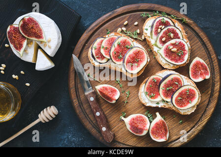 La bruschetta avec des figues violettes, ricotta et miel sur planche à découper en bois servi avec fromage brie camambert et décoré avec du thym. Banque D'Images