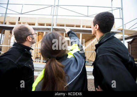 Vue arrière du female carpenter orienté vers la construction incomplète en position debout par des collègues Banque D'Images