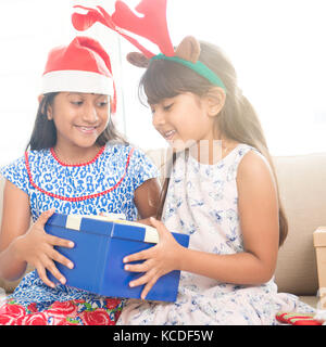 Happy indian family celebrating christmas holidays, avec boîte-cadeau et santa hat sitting on sofa at home, cute asian festival des enfants sur l'humeur. Banque D'Images