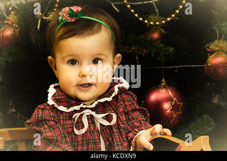 Petite fille est assise sur le cheval de bois en face de l'arbre de Noël, effet vintage photo Banque D'Images