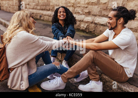 Les jeunes gens assis ensemble et se tenant la main dans la joie. Amis avec leurs mains empilées montrant l'unité et de l'équipe. Banque D'Images