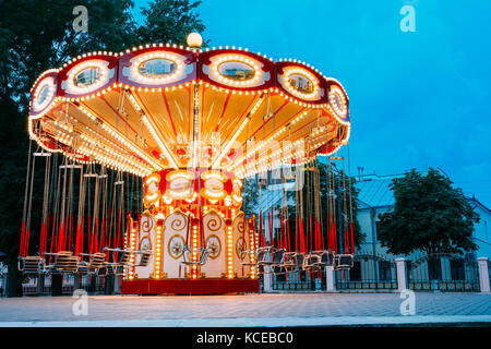 L'éclairées carrousel vide merry-go-round avec sièges suspendus sur les chaînes sans les personnes en attente de ses visiteurs. Soirée d'été en ville Banque D'Images