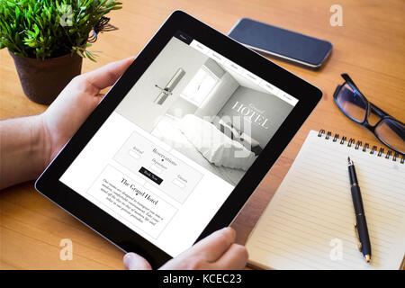 Mains d'un homme tenant une tablette montrant site de l'hôtel. Tous les graphiques de l'écran sont constitués. Banque D'Images