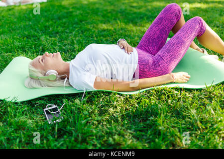 Photo de jeune fille de l'athlète dans les écouteurs sur la pelouse pendant la journée Banque D'Images