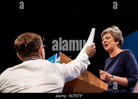 Manchester, Royaume-Uni. 4 octobre 2017. Un manifestant (l) remet à la première ministre britannique Theresa May une note P45 lors de son discours à la conférence à Manchester. Le discours de la première ministre britannique Theresa May à Manchester a été interrompu mercredi par un manifestant. Un homme s'est approché de l'avant de la salle et a remis à May une note P45, une lettre remise lorsque les emplois des gens sont terminés. Crédit : Han Yan/Xinhua/Alamy Live News Banque D'Images