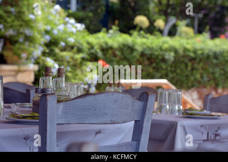 Quelques chaises poussées sous une table au restaurant ou une taverne grecque avec des lunettes et des condiments set ready pour diners. Spéciaux et des couverts sur une table. Banque D'Images