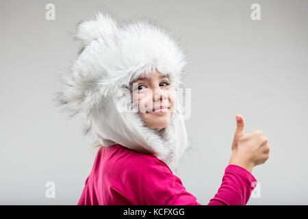 Portrait of smiling preteen girl wearing cap hiver moelleux giving thumb up contre fond uni Banque D'Images