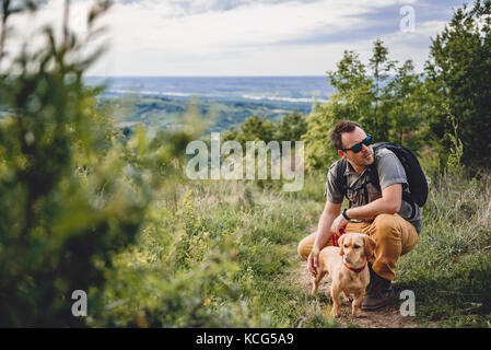 L'homme portant des lunettes de soleil avec un petit chien jaune se reposant à la sentier de randonnée pédestre Banque D'Images