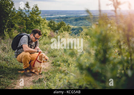 L'homme portant des lunettes de soleil avec un petit chien jaune se reposant à la sentier de randonnée pédestre Banque D'Images