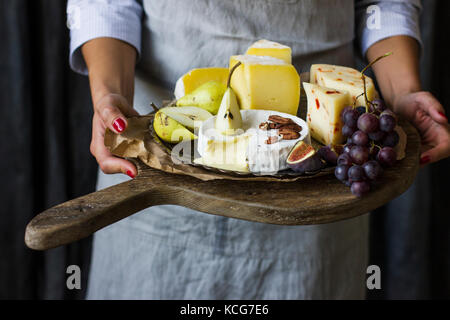 Jeune femme maintenant la plaque de fromage sur la planche de bois Banque D'Images