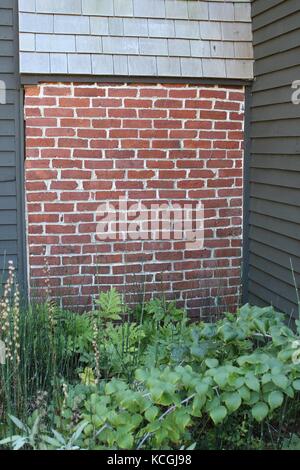 Un mur de briques avec un toit en bardeaux et un petit petit jardin avec plantes verte à côté d'elle Banque D'Images