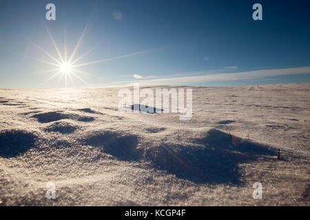 La neige sur la surface inégale de champs agricoles. Le soleil scintille à neige. formé d'ombres. Il y a une colline. dans le contexte de l'blue Banque D'Images