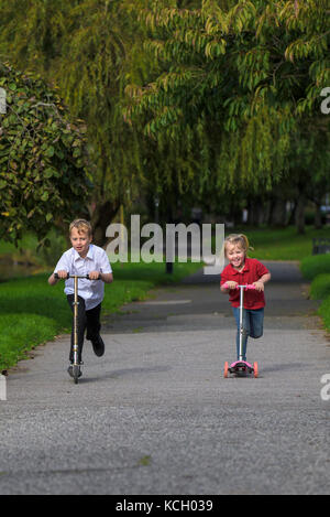 Les enfants qui voyagent en scooter - un jeune garçon et sa jeune sœur qui s'amusent à courir le long d'un chemin sur leurs scooters. Banque D'Images