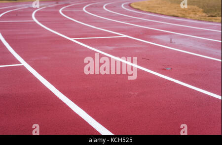 Des lignes blanches de la marque de voie sur une piste de course rouge usé. Banque D'Images