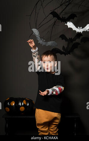 Petit garçon sur Halloween party sur fond noir avec des citrouilles et des chauves-souris sur un arbre Banque D'Images