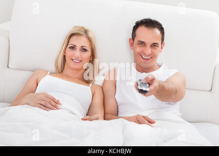 Couple Relaxing on lit avec une télécommande dans la main à regarder la télévision Banque D'Images