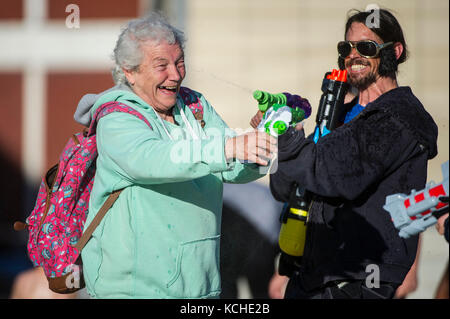 Une vieille femme et un homme en robe de soirée avec les pistolets à eau prendre part à un combat de l'eau à Bristol la place du millénaire. Banque D'Images