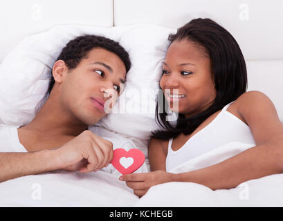 Portrait of young couple in bed holding heart Banque D'Images