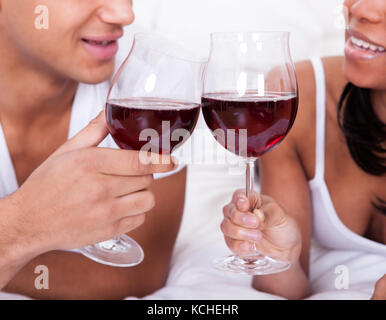 Portrait of young couple toasting with red wine on bed Banque D'Images