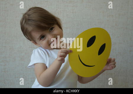 Un enfant tenant un cercle jaune avec sourire émoticône face au lieu de la tête. Banque D'Images