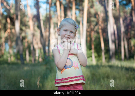 Peu de belle fille blonde dans la forêt. elle sourit Banque D'Images