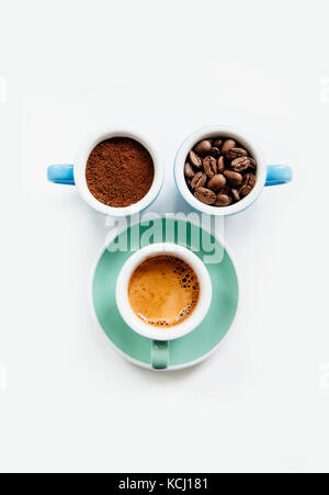 Trois tasses de café : café moulu (poudre), les grains de café et espresso fraîchement préparés dans des tasses en céramique colorée (bleu et vert menthe) sur le livre blanc Banque D'Images