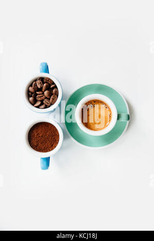 Trois tasses de café : café moulu (poudre), les grains de café et espresso fraîchement préparés dans des tasses en céramique colorée (bleu et vert menthe) sur le livre blanc Banque D'Images