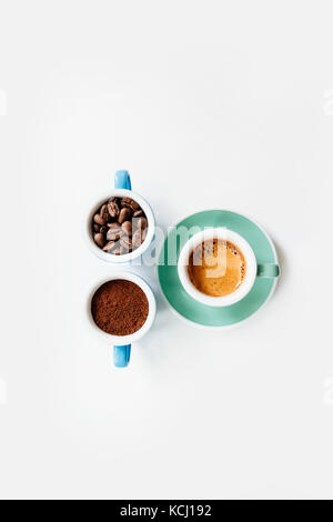 Trois tasses de café : café moulu (poudre), les grains de café et espresso fraîchement préparés dans des tasses en céramique colorée (bleu et vert menthe) sur le livre blanc Banque D'Images