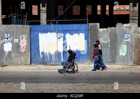 Homme handicapé en fauteuil roulant sur la chaussée devant le chantier, El Alto, Bolivie Banque D'Images