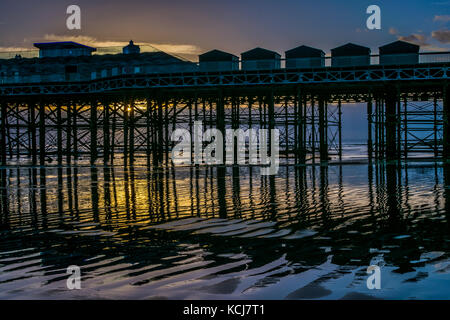 Structure en fer hastings pier reflétée dans le sable humide au coucher du soleil et à marée basse Banque D'Images