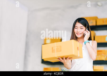 Propriétaire de petite entreprise, asian woman hold package fort, à l'aide de mobile téléphone recevoir une commande d'achat, travailler au bureau à domicile. Livraison de marketing en ligne Banque D'Images