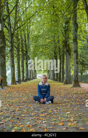 Jeune fille blonde assise sur le sol entre les arbres Banque D'Images