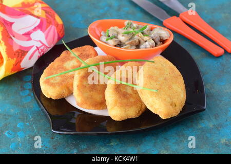 Galettes de pommes de terre sur une plaque noire avec sauce crémeuse aux champignons dans un bol d'orange sur un fond vert abstrait Banque D'Images