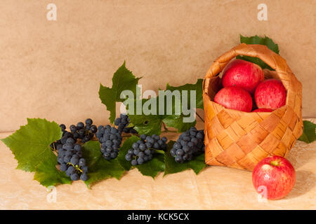 Alimentation saine. fresh fruits mûrs pommes rouges dans panier en osier avec des feuilles et des raisins sur table close up. Banque D'Images