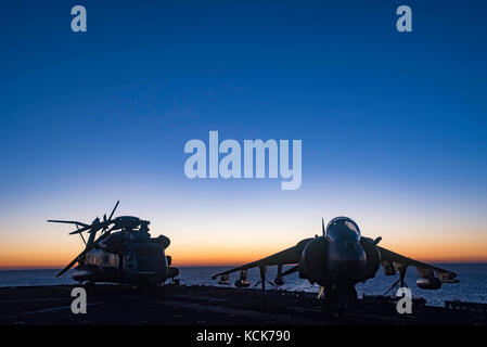 Un hélicoptère CH-53E Super Stallion du corps des Marines des États-Unis (à gauche) et un avion d'attaque au sol AV-8B Harrier II sont assis sur le pont d'envol du navire d'assaut amphibie USS Bonhomme Richard de classe Wasp de la marine des États-Unis au coucher du soleil le 29 juillet 2017 dans la mer de Corail. (Photo de William Sykes via Planetpix) Banque D'Images